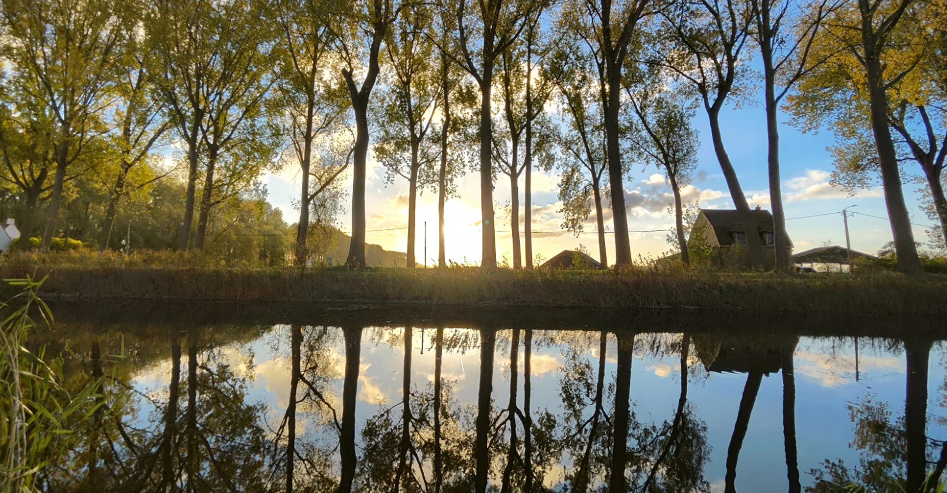 Tree lined canal, with farm buildings and the sun rising in the background