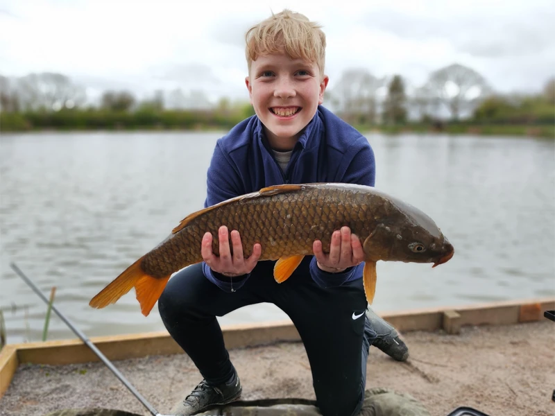 Young person holding carp with lake in the background